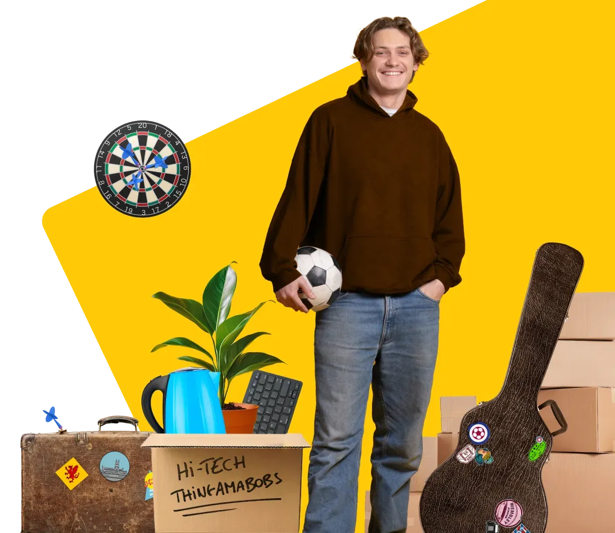 Student standing alongside belongings to be moved (dartboard, cardboard box, guitar case, suitcase, house plant)